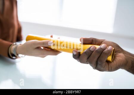 Close-up Of Businessman's Hand Passing The Golden Baton To His Partner In Office Stock Photo