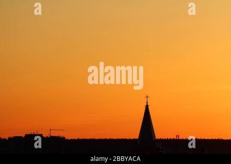 Sun below the horizon and the roof of the church with a cross on the background fiery dramatic orange sky at sunset or dawn backlit by the sun. Place for text and design. Stock Photo