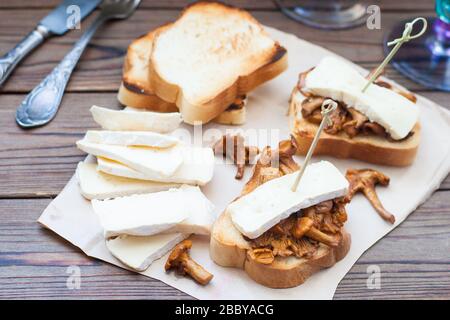 Two bruschettas with brie and chanterelle mushrooms, on wooden table with fork and knife on white napkin Stock Photo