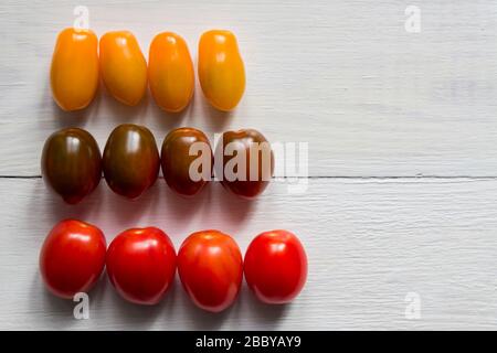 Three rows of different sorts of cherry tomatoes. Yellow, red and green. Organic ripe tomato on wooden table, top view Stock Photo