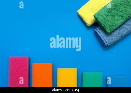 Three colorful, dry microfiber cloths and rainbow colored sponges for cleaning various surfaces in the kitchen, bathroom and other rooms, on a blue ba Stock Photo