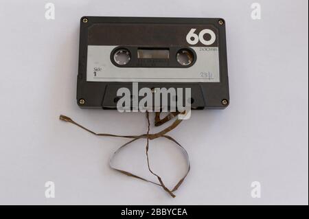 Broken tape spills out the bottom of an analogue cassette tape Stock Photo