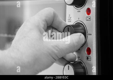 Man setting the power setting on an electric oven grill by turning a dial.  With selective colour Stock Photo
