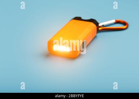 An orange led flashlight with a carabiner glows on a blue background. Stock Photo