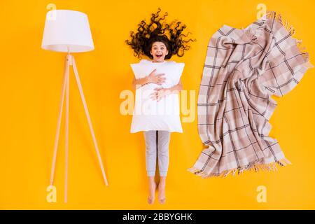 Full size high angle above flat lay view photo of funny brunette little lady lying comfy bedroom hug pillow near plaid blanket lamp wear pajama Stock Photo