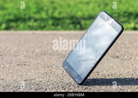 Black modern smartphone falls on the asphalt at the corner of the screen. A cell phone with a cracked, smashed, broken screen with copy space. Stock Photo