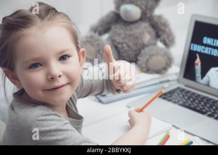 little girl uses laptop to learn from home. The child smiles happily and gets knowledge remotely. digital concept e-learning Stock Photo