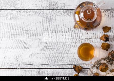 Chaga mushrooms infusion in glass teapot on white wooden board. Trendy healthy beverage. Top view. Useful coffee alternative to boost immunity during Stock Photo