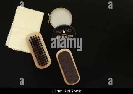 Brush, soft cloth, dubbin wax paste and coarse grade sandpaper as vintage boot care kit or shoe shine kit accessories on black background from above. Stock Photo