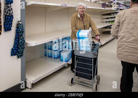 Elderly lady in supermarket with large pack of toilet roll in her shopping basket during Coronavirus panic buying in UK March 2020 Stock Photo