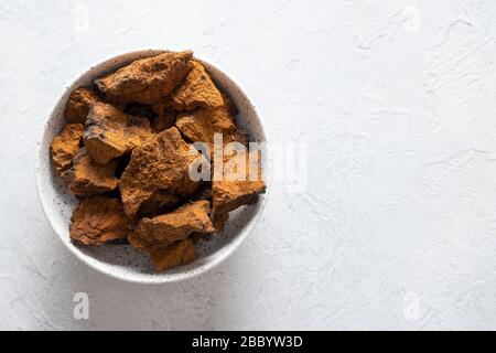 Chaga Birch Mushrooms in bowl on light table. Trendy healthy superfood for infusion, tea or coffee. Horizontal. Copy space. Stock Photo
