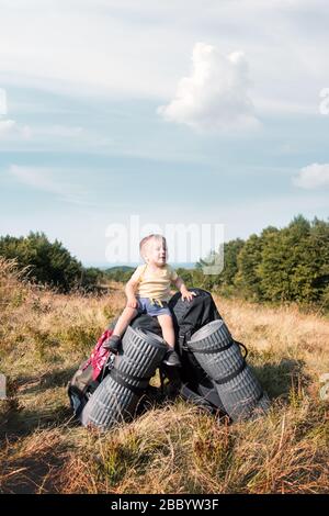 Small kid sitting on tourists backpacks in autumn mountains. Travel concept Stock Photo