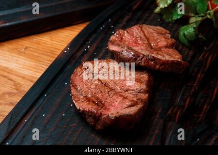 Thick juicy portions of fried fillet steak are served, sprinkled with salt, on an old wooden board. The dish is ready to serve. Stock Photo