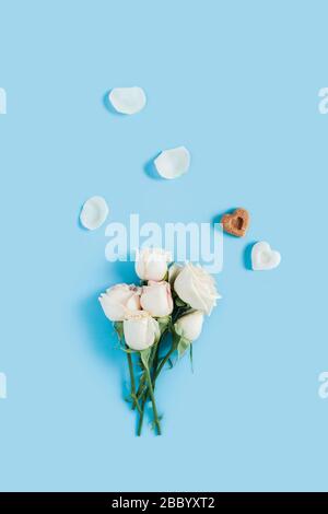 Vertical morning card. White roses on a blue background with scattered petals and two pieces of sugar in the shape of hearts. Stock Photo