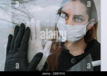 woman in quarantine seeing her fried who came to visit her due to coronavirus covid-19 wit mask and gloves on window at home