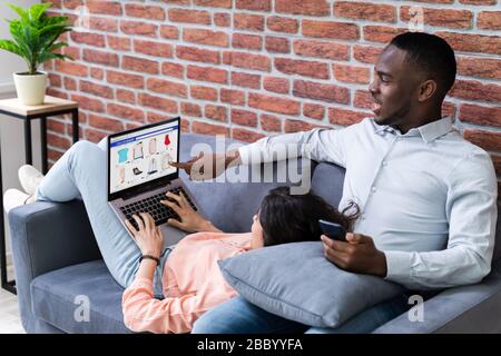 Couple Using Laptops While Relaxing On Sofa At Home Stock Photo