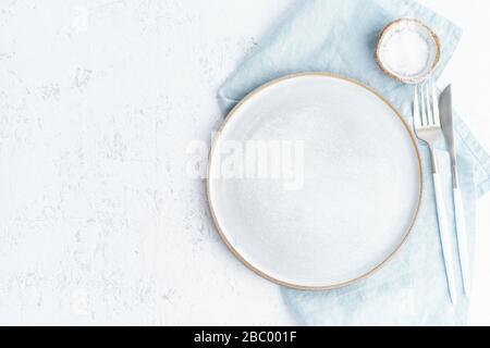 Clean empty white ceramic plate, fork and knife on white stone table, copy space, Stock Photo