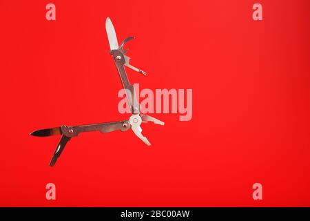 Multitool is a multi-functional tool on a red background. The concept of an open, flying multi-tool with free space. Stock Photo