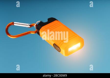 An orange led flashlight with a carabiner glows on a blue background. Stock Photo