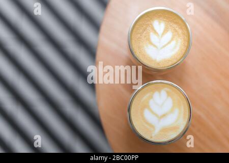 Coffee with a pattern on a foam in two glasses. Against the background of the table and striped tiles in blur. Photo taken from above. Stock Photo