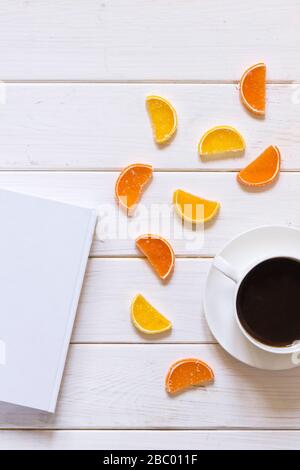 white cup of coffee, white paper and multicolored fruit marmalade lie on a white wooden background Stock Photo