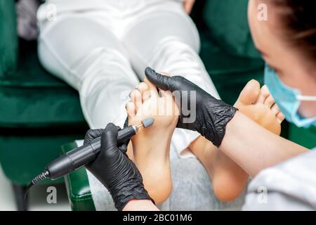Pedicure master polishes foot of woman with special machine tool close up.
