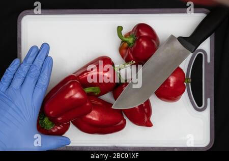 Man in Hygiene Gloves Cuts Red Sweet Peppers At Home With Knife, Precaution against Corona Virus 2020 Stock Photo