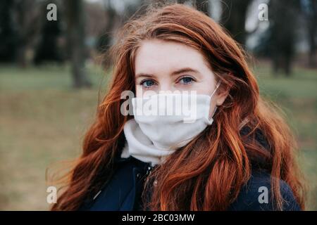 Portrait of beautiful woman with red hair walking on the street wearing protective mask outdoors.