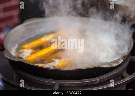 Street food. Boiling corn in a large cauldron, and thick boiling water rises above boiling water. On the street in the city. Stock Photo