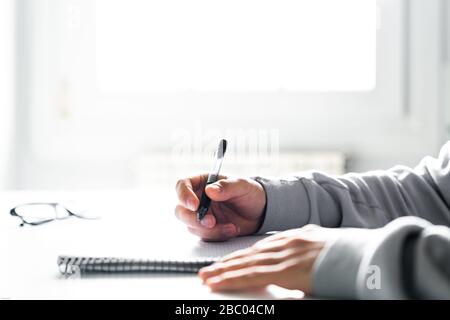 Student writing in a notebook doing homework at his desk at home Stock Photo