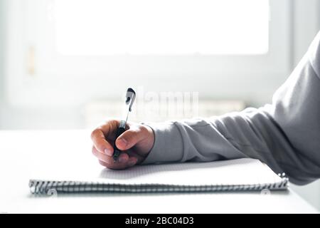 Young man writing in a notebook doing homework at his desk at home Stock Photo