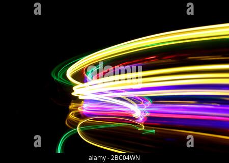 Long exposure photo of neon multicolored light in an abstract swirl, parallel lines pattern against a black background. Light painting photography. Stock Photo