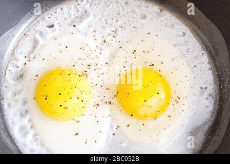 fried eggs with spices on the black pan close-up. two eggs Stock Photo