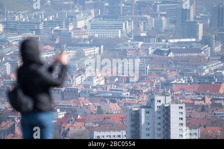 Stuttgart, Germany. 02nd Apr, 2020. A woman is standing with her smartphone on top of Birkenkopf and looking at the view of the city centre. More than 15,000,000 cubic meters of rubble were deposited on the hill after the Second World War. The mountain is popularly known as 'Monte Scherbelino'. Credit: Marijan Murat/dpa/Alamy Live News Stock Photo