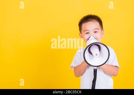 Asian Thai happy portrait cute little cheerful child boy holding and shouting or screaming through the megaphone her looking to camera, studio shot is