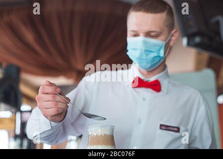 the waiter works in a restaurant in a medical mask Stock Photo