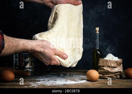 Pizza dough cooking in the home kitchen. Homemade dough for bread, pizza, pastries and rolls. Dough ingredients (flour, eggs, butter) on a wooden rust Stock Photo