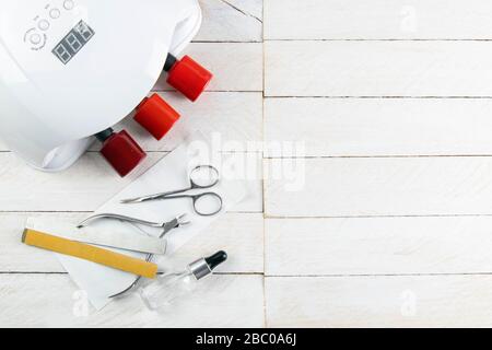 A set of cosmetic tools for manicure and pedicure on a blue background. Manicure lamp, varnish gel, manicure scissors, cuticles and white towel stand Stock Photo