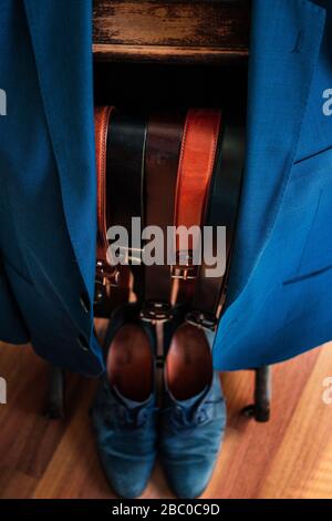 A Jacket on a coat hanger with several belts to choose from and matching shoes at the bottom. Suit, Business, style, fashion, clothing, outfit Stock Photo