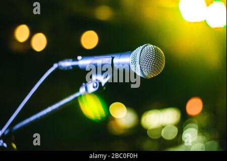 singer's vocal microphone stands on stage during a concert with multi-colored lights on the background Stock Photo