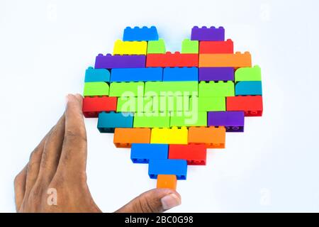 A person making a heart shape with lot of different colored building blocks in front of a n isolated white background Stock Photo