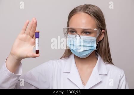 Young woman holding test tubes with blood and antidote in her hand. Coronavirus blood Test tube. Positive Blood Sample in Scientist Hand. Stock Photo