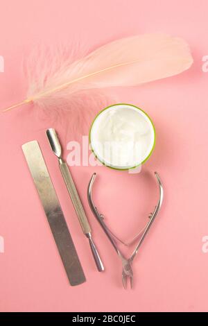 Manicure scissors, cuticle bag, nail polish and hand cream together with a pink pen stand on the pink table. Stock Photo