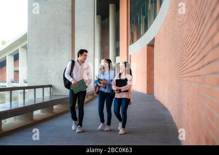 Asian three students are walking and talking together in university hall during break in University. Education, Learning, Student, Campus, University, Stock Photo