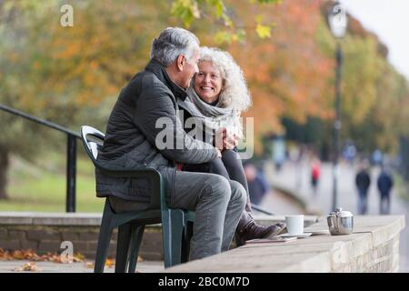 Smiling, affectionate active senior couple drinking tea in autumn park Stock Photo