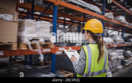 Female factory worker with clipboard checking inventory in warehouse Stock Photo