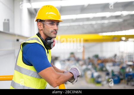 Serious male supervisors leaning on platform railing in factory Stock Photo