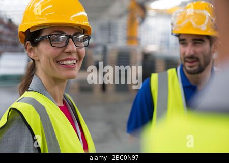 Smiling female worker talking with coworkers in factory Stock Photo