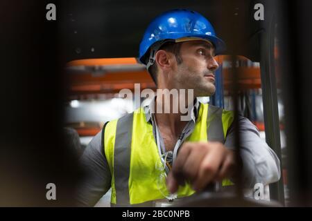 Male worker driving forklift, looking over shoulder in factory Stock Photo