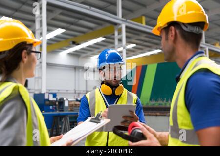 Supervisor and workers with clipboard and digital tablet talking in factory Stock Photo
